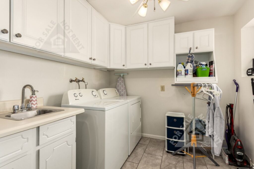 Laundry room in Sunland Village home with multiple storage cabinets, sink, and included washer and dryer